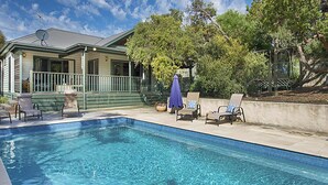 A swimming pool with lounge chairs and an umbrella, surrounded by a house and trees. - Poolside Sorrento (SORRENTO)