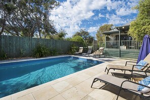 A swimming pool with clear blue water, surrounded by lounge chairs and a wooden fence. - Poolside Sorrento Pet Friendly (SORRENTO)