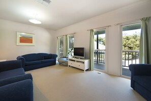 A living room with a blue sofa, a television on a white stand, and a painting on the wall. - Poolside Sorrento Pet Friendly (SORRENTO)