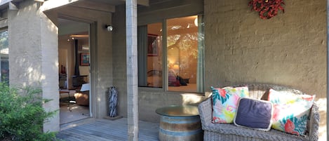 A covered porch with a wicker sofa, a round table, and a decorative wall piece.