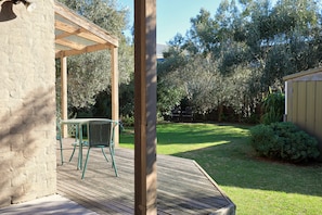 Een houten terras met een pergola, een tafel en een stoel.
