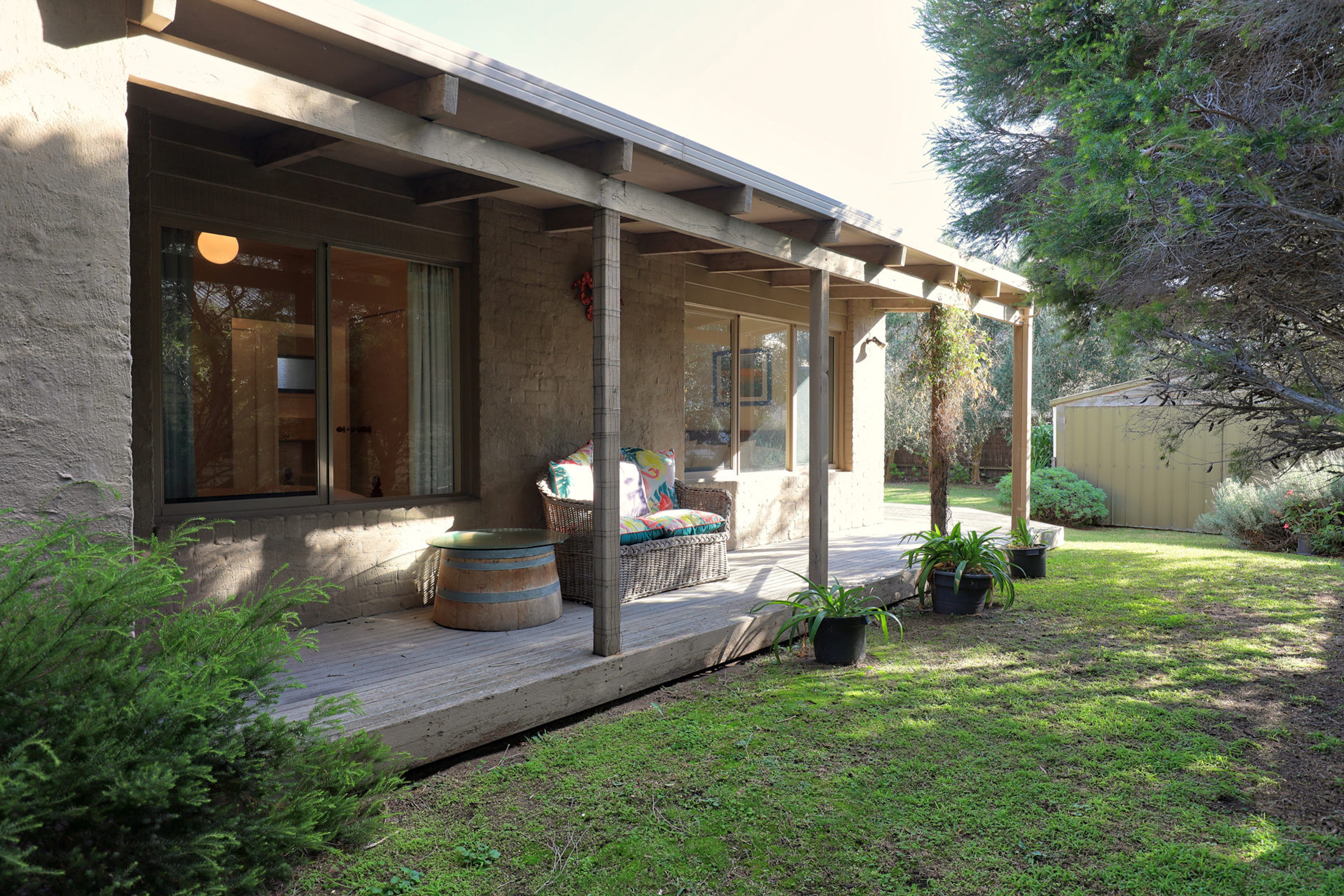 A covered outdoor area with a wooden deck, a seating area with cushions, and potted plants.