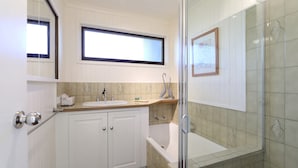 Een badkamer met een wit wastafelmeubel, een bad en een douchehoek.