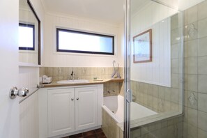 Een badkamer met een wit wastafelmeubel, een bad en een douchehoek.
