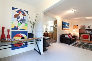 A modern living room with a glass coffee table, a black leather sofa, and a dining area with a wooden table and chairs. - Back Beach Hideaway Blairgowrie (BLAIRGOWRIE)