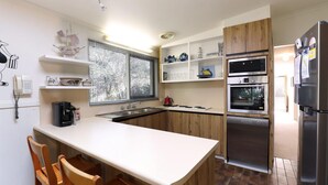 A modern kitchen with a central island, wooden cabinets, stainless steel appliances, and a window with blinds. - Back Beach Hideaway - Family friendly beach house (BLAIRGOWRIE)