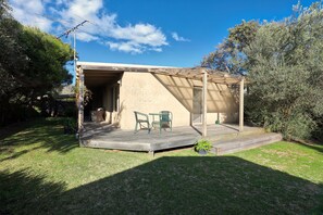 A covered outdoor seating area with a table and chairs, a wooden deck, and a brick wall. - Back Beach Hideaway Blairgowrie (BLAIRGOWRIE)