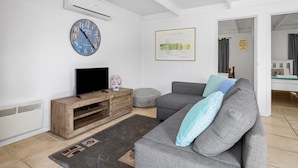 A modern living room with a grey sofa, a flat-screen TV on a wooden stand, a large wall clock, and a framed map.