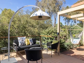 Een terras buiten met een bank, stoelen, een hangstoel en een lamp.