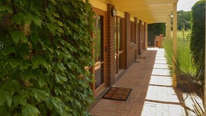 A covered walkway with brick flooring, a door with a doormat, and a wall with climbing ivy.