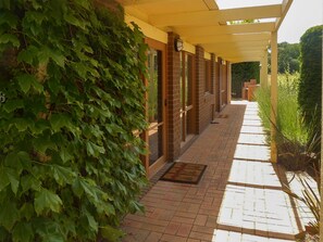 A covered walkway with brick flooring, a door with a doormat, and a wall with climbing ivy. - Quarterdeck Portsea Coastal Pet Friendly Escape (PORTSEA)