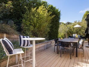 An outdoor deck with a round table and chairs, surrounded by greenery and trees. - Quarterdeck Portsea Coastal Pet Friendly Escape (PORTSEA)