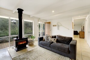 A modern living room with a fireplace, a sofa, and a view of the outdoors. - Quarterdeck Portsea Coastal Pet Friendly Escape (PORTSEA)