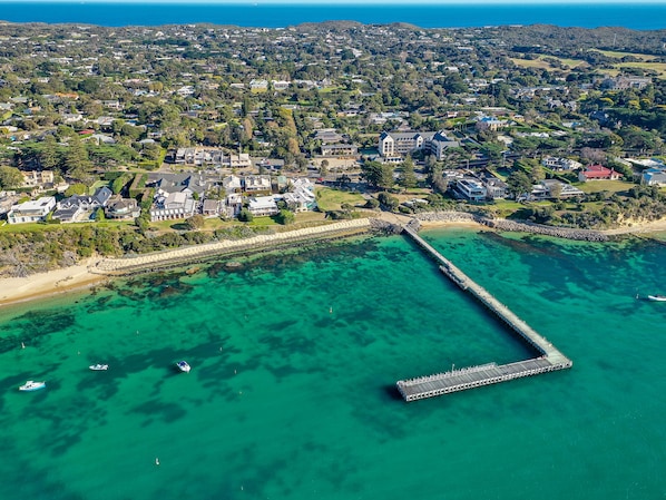 Luchtbeeld van een kustwoongebied met een opvallende pier die zich uitstrekt in het turquoise water.