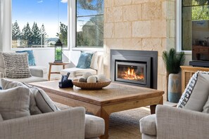 A cozy living room with a fireplace, comfortable seating, and a view of trees.