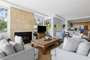 A modern living room with a fireplace, comfortable seating, and a view of the outdoors. - Koonya Paradise Sorrento Home with Pool and Views (SORRENTO)