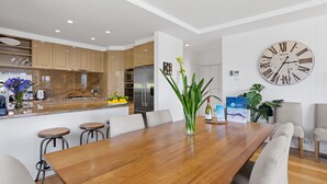 Une cuisine moderne dotée d’un îlot central, d’appareils électroménagers en acier inoxydable et d’un coin repas avec une table et des chaises en bois.