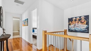 Un corridoio con pavimento in legno, una scala con ringhiera in legno e un quadro raffigurante tre figure su una barca appeso al muro.