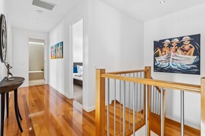 Un pasillo con piso de madera, una escalera con barandilla de madera y un cuadro en la pared que muestra tres figuras en un bote.