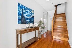 Un escalier en bois avec une rampe, une console ornée de quelques objets décoratifs et un grand tableau accroché au mur.