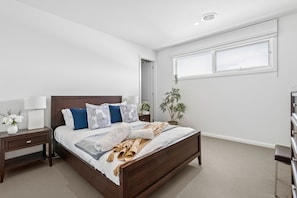 Un dormitorio con una cama de madera, una mesita de noche, una lámpara, una planta en maceta y una ventana.