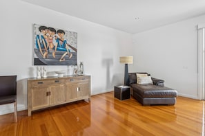 Un soggiorno moderno con pavimento in legno, un divano in pelle marrone, un mobile in legno e un quadro con tre figure.