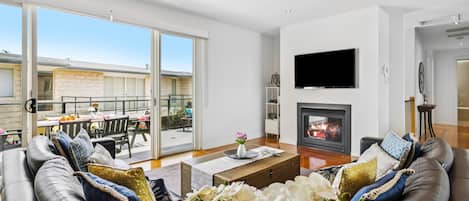 A spacious living room with a fireplace, a flat-screen TV, and a balcony with outdoor furniture.