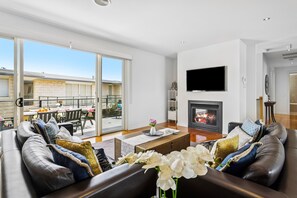 Un salón amplio con chimenea, televisor de pantalla plana y balcón con mobiliario exterior.