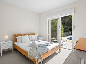 A bedroom with a bed, bedside tables, a lamp, and a view of an outdoor area through a sliding glass door. - Bluetopia Spacious Rye Retreat with Pool and BBQ (RYE)