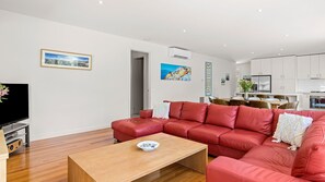 Un salon moderne avec un canapé en cuir rouge, une table basse en bois et un téléviseur à écran plat. Il y a également un coin cuisine avec des meubles blancs et une table à manger avec des chaises.
