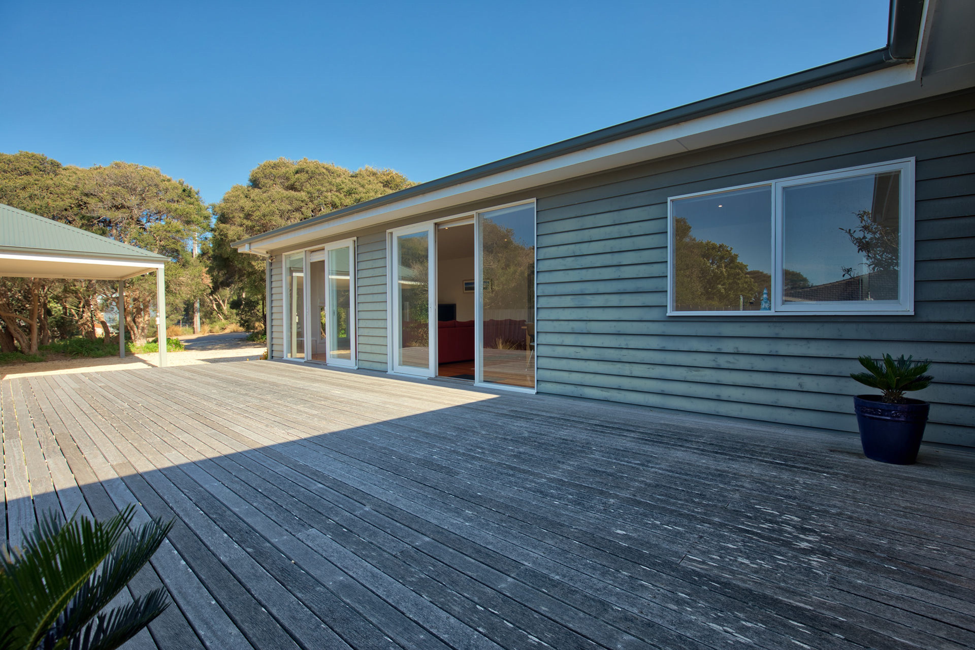 A modern house with a wooden deck, large sliding glass doors, and a potted plant.
