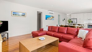 A modern living room with a red leather sofa, a wooden coffee table, and a flat-screen TV on a stand. - Bluetopia Spacious Rye Retreat with Pool and BBQ (RYE)