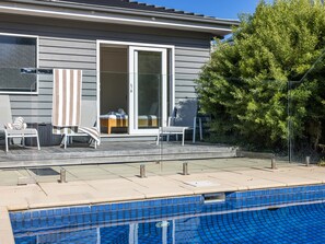 A residential property with a swimming pool, a covered patio with seating, and a sliding glass door leading to a bedroom. - Bluetopia Spacious Rye Retreat with Pool and BBQ (RYE)