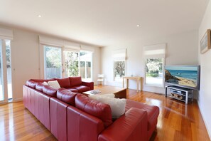 Un salon spacieux avec un canapé en cuir rouge, une table basse et un téléviseur diffusant une scène de plage.