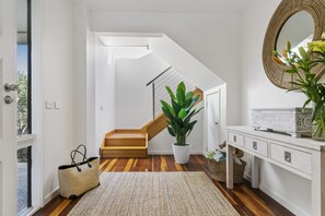 A modern interior with a staircase, a potted plant, a wicker basket, and a white console table. - Dunescape Spacious Rye Retreat with Private Pool (RYE)