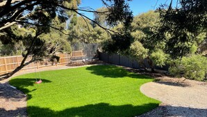 A backyard with a green lawn, a trampoline, and a wooden fence. - Dunescape Spacious Rye Retreat with Private Pool (RYE)