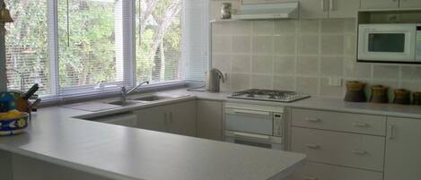 A kitchen with a built-in stove, microwave, and sink. There are wooden stools and a window with blinds.