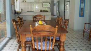 A dining room with a wooden table and chairs, a kitchen in the background, and a patterned floor. - Blairgowrie Relaxation (BLAIRGOWRIE)