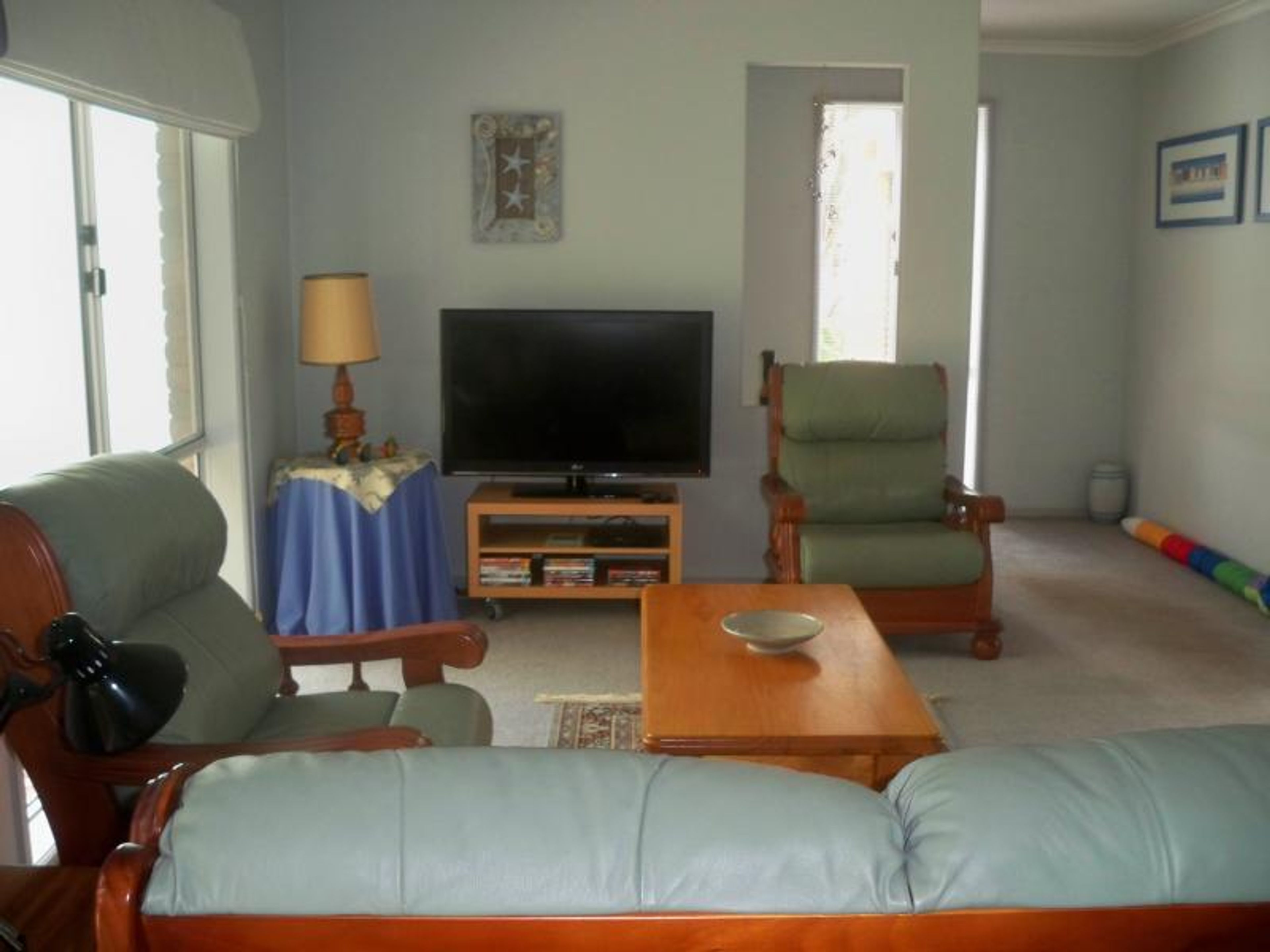 Uma sala de estar com televisão, sofá, poltrona, mesa de centro e abajur.