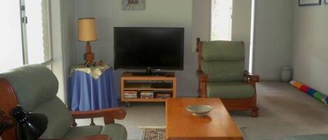 Uma sala de estar com televisão, sofá, poltrona, mesa de centro e abajur.
