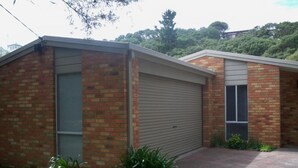 A two-story brick building with a garage door, a small front yard with grass and plants, and a driveway leading to the garage. - Blairgowrie Relaxation (BLAIRGOWRIE)