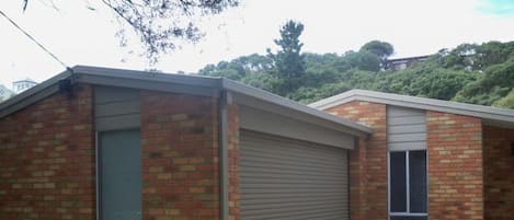 A two-story brick building with a garage door, a small front yard with grass and plants, and a driveway leading to the garage.