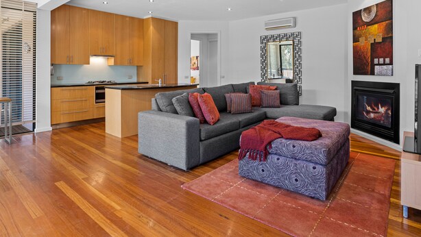 A modern living space with a grey sofa, ottoman, wooden cabinets, and a fireplace. - Diamond View Sorrento Holiday Home with Pool (Sorrento)