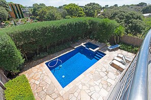 A swimming pool with stone tiles and a surrounding hedge.