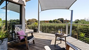 An outdoor deck with wooden furniture, a table with a bottle, and a view of the surrounding landscape. - Diamond View Sorrento Holiday Home with Pool (Sorrento)