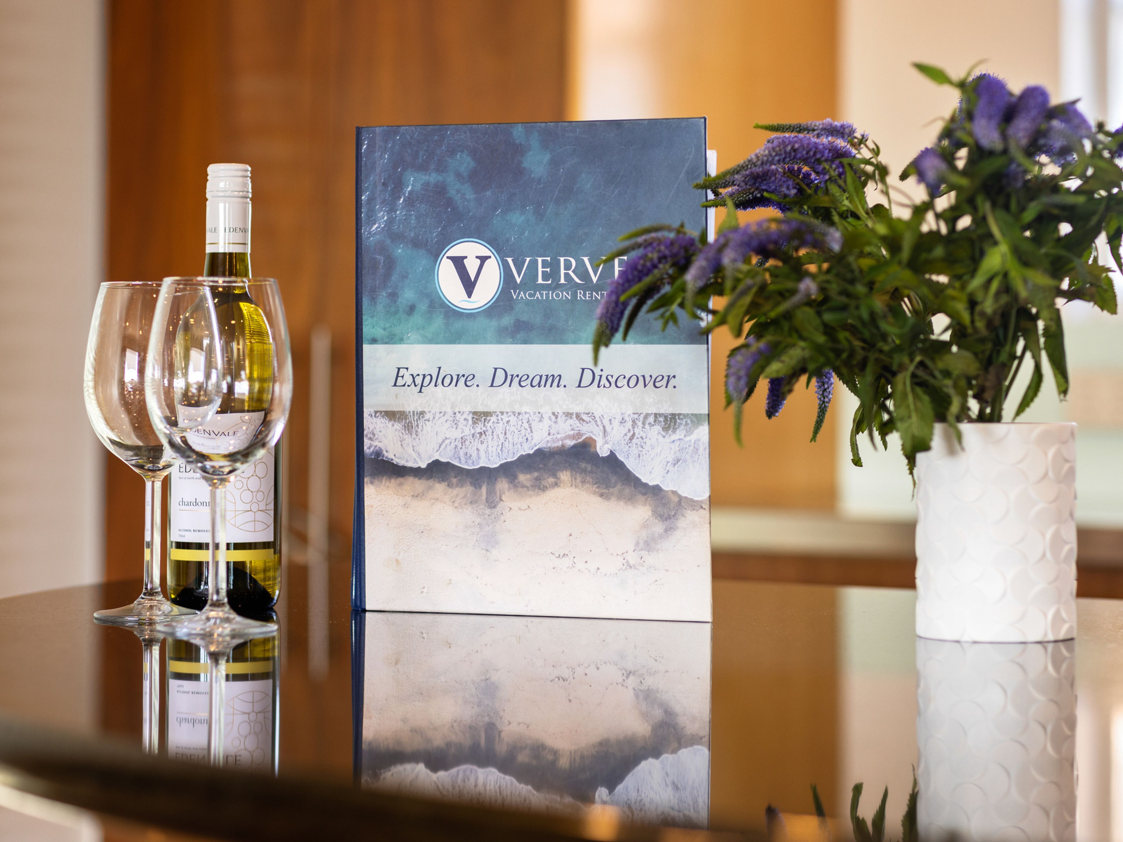 A table with two wine glasses, a bottle of wine, a brochure, and a potted plant.