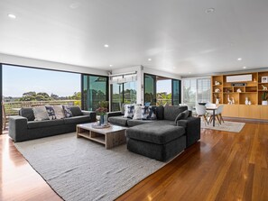 A modern living room with a large window, grey sofas, a coffee table, and a wooden cabinet with decorative items.