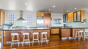 A modern kitchen with wooden cabinets, a stainless steel refrigerator, and a bar area with stools. - Diamond View Sorrento Holiday Home with Pool (Sorrento)