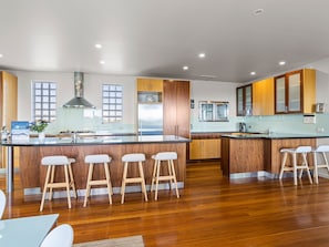 A modern kitchen with wooden cabinets, a stainless steel refrigerator, and a bar area with stools. - Diamond View Sorrento Holiday Home with Pool (Sorrento)