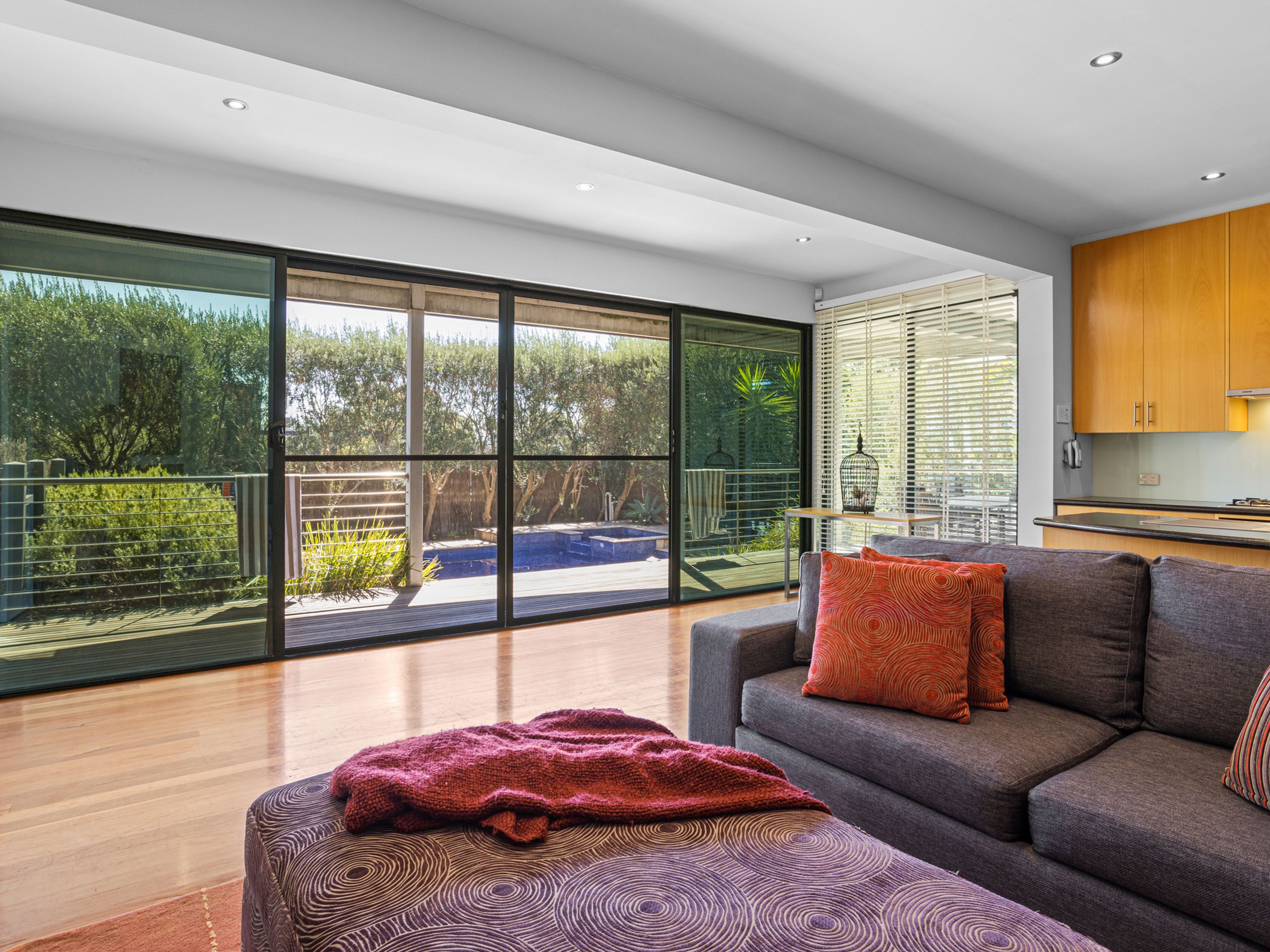 Een moderne woonkamer met een grote schuifpui naar een balkon, een grijze bank met decoratieve kussens en een houten vloer.